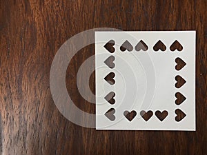 Punched in heart shape of white square blank paper on dark brown wood table